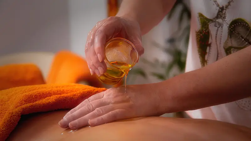 Praticienne versant de l'huile tiède sur le dos d'une personne lors d'un massage ayurvédique