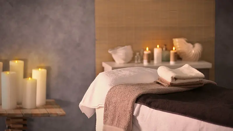 Table de massage habillée de draps avec une pile de serviettes pliées, dans un cabinet tamisé éclairé aux bougies