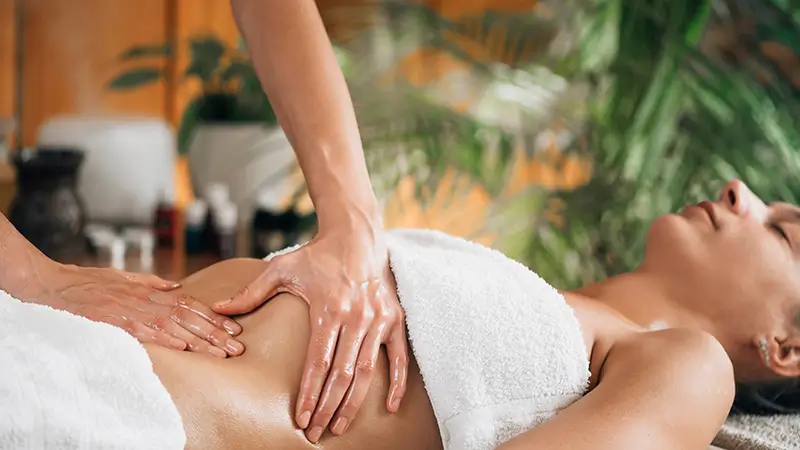 Praticienne réalisant un massage à l'huile sur le haut du buste d'une femme allongée lors d'un soin ayurvédique
